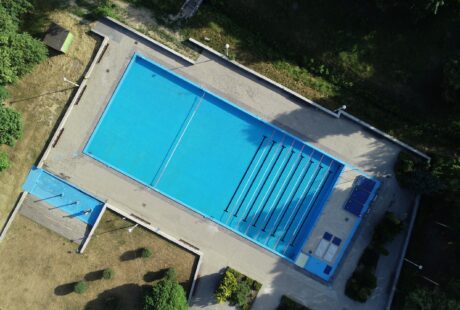 Widok z lotu ptaka na odkryty basen z torami do pływania, otoczony tarasami i zielonymi drzewami.