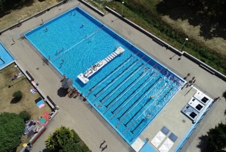 Widok z lotu ptaka na kompleks odkrytych basenów z torami do pływania, płytkim basenem, leżakami i pływającymi ludźmi.