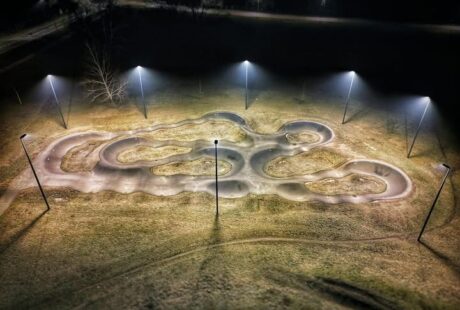 Widok z lotu ptaka na oświetlony nocą tor do jazdy typu pumptrack na świeżym powietrzu, z krętymi ścieżkami i otoczony trawiastym terenem.