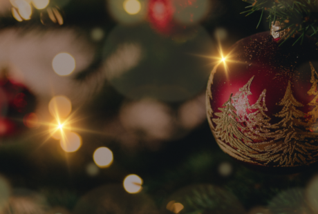Zbliżenie na udekorowaną choinkę z czerwoną ozdobą ze złotymi wzorami, otoczoną delikatnymi światłami i rozmytym świątecznym tłem.