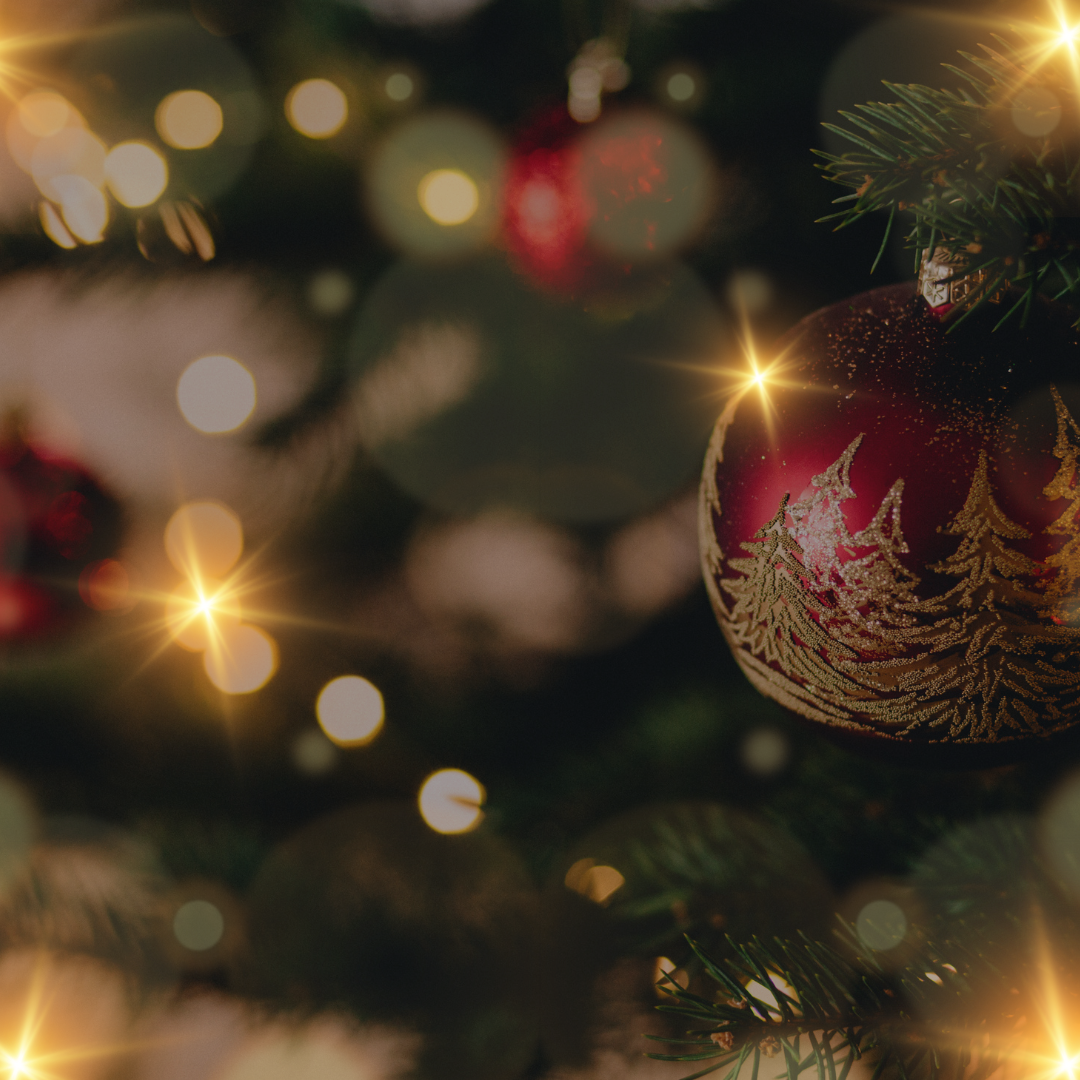 Zbliżenie na udekorowaną choinkę z czerwoną ozdobą ze złotymi wzorami, otoczoną delikatnymi światłami i rozmytym świątecznym tłem.